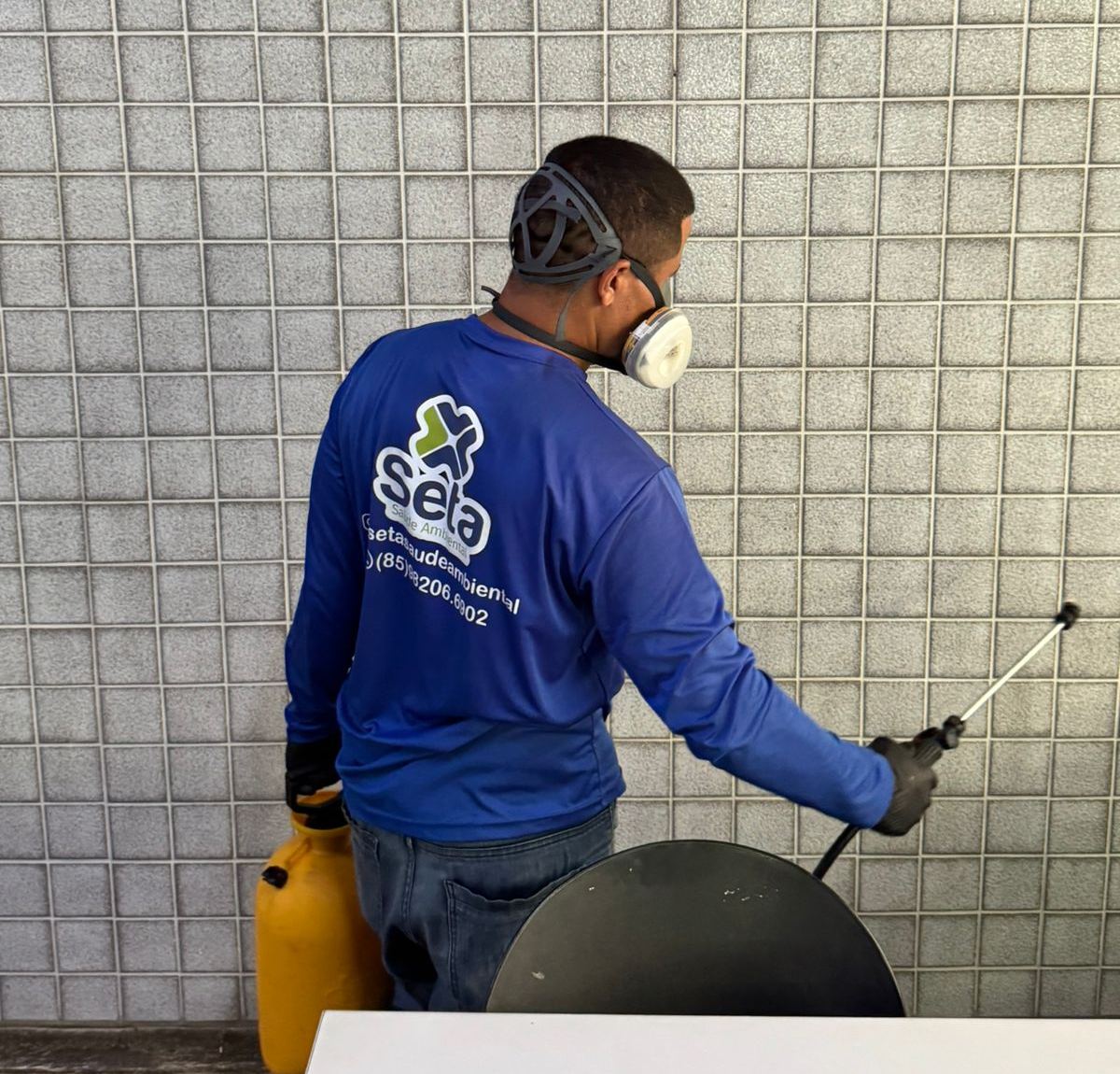 Técnico da SETA Saúde Ambiental, de uniforme e máscara de proteção, aplicando produto para controle de pragas na parede de um imóvel